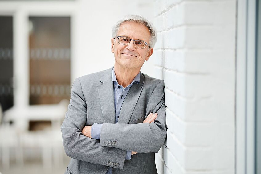 Professor Prenzel lehnt an einer weißen Ziegelwand