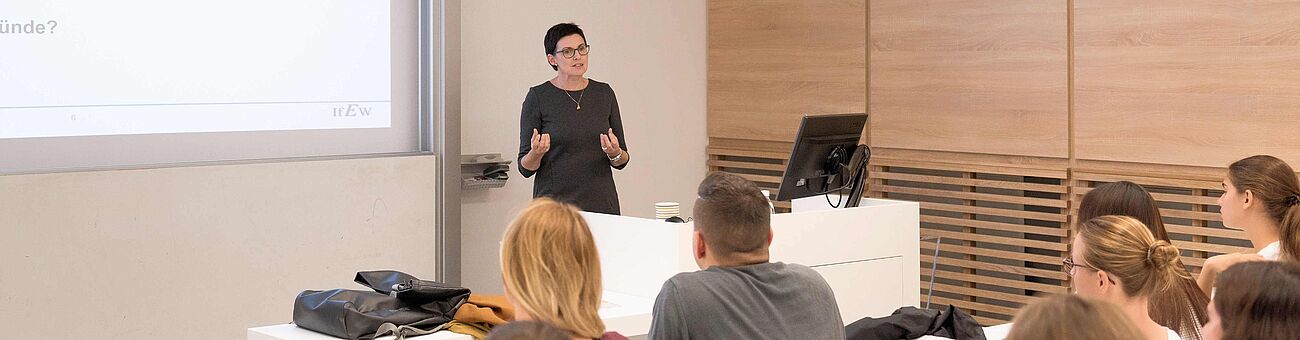 a lecturer is standing behind a lecture desk and students listening