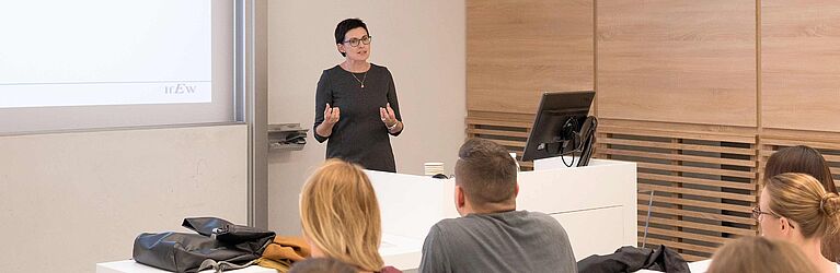 a lecturer is standing behind a lecture desk and students listening